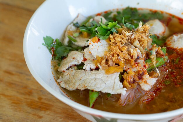 Rice noodle in spicy soup with pork ball, vegetable and pork serving on wooden desk in canteen