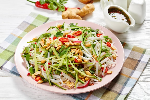 Tagliatelle di riso e insalata di verdure su un piatto su un tavolo di legno con condimento in una salsiera, cucina asiatica, vista orizzontale dall'alto