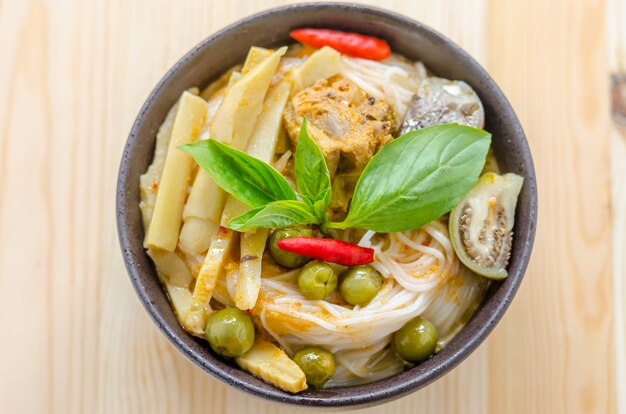 Rice noodles in chicken curry sauce with vegetables on wooden background