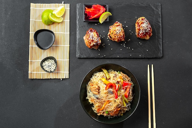 Photo rice noodles or crystal with other asian food on a dark background teriyaki chicken and roasted kore