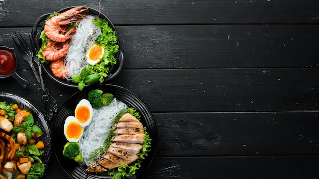 Rice noodles dishes in black plate on black background Asian cuisine Top view Free space for your text