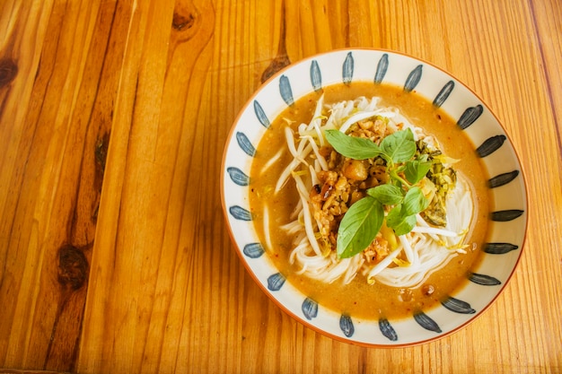 Rice noodles in fish curry sauce with vegetables on a wooden table and plate