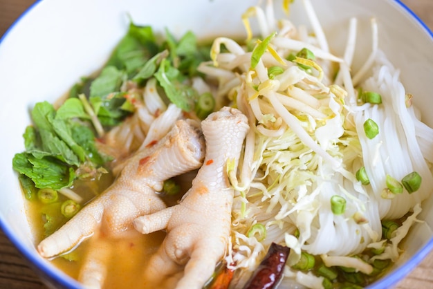 Rice noodles with chicken feet on soup bowl on wooden table food background Thai food thai rice noodles spicy soup curry with fresh vegetable