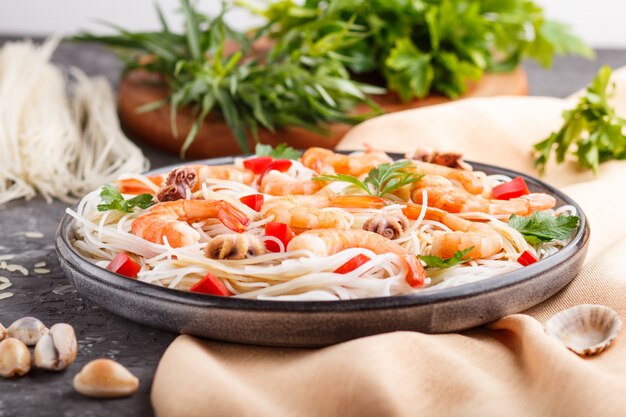 Rice noodles with shrimps or prawns and small octopuses on gray ceramic plate on a black concrete background