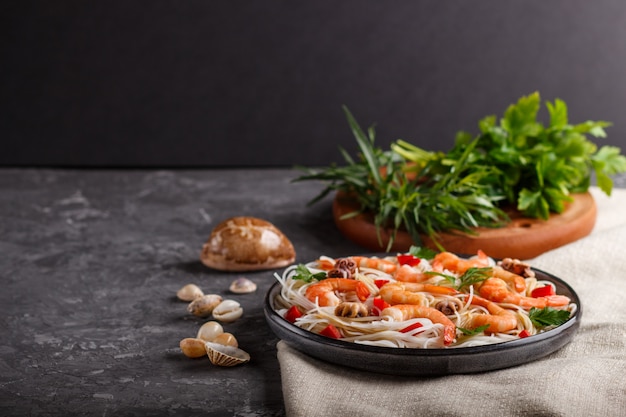 Rice noodles with shrimps or prawns and small octopuses on gray ceramic plate on a black concrete . side view, copyspace.