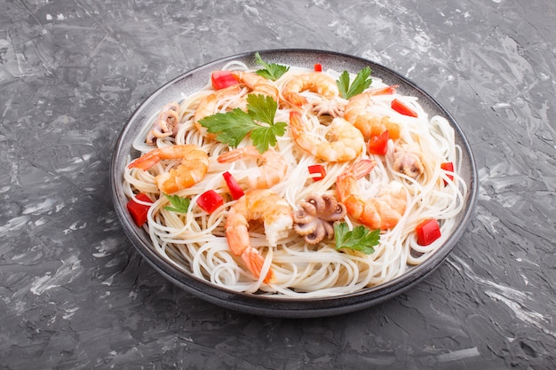 Rice noodles with shrimps or prawns and small octopuses on gray ceramic plate on a black concrete . Side view.