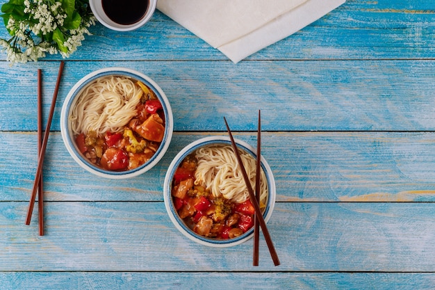 Rice noodles with stir-fried chicken and vegetables in bowls and chopsticks