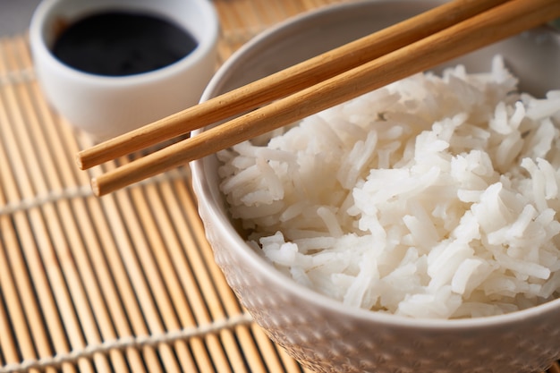 Rice in a porcelain bowl, with Japanese chopsticks, soy sauce, served on a gray stone table Close up