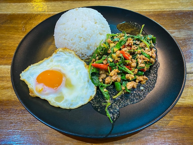 Rice topped with stirfried pork and basil with a fried egg on the table