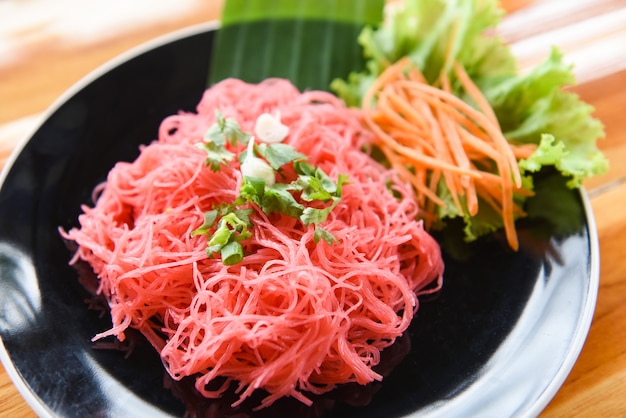 米春雨のピンクのフライパンと野菜の炒めた赤米炒め麺は、木製のテーブルのプレートで提供していますタイ風アジアンヌードル