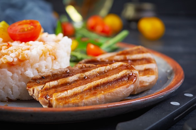 Rice with grilled pork meat, tomatoes and green herbs on dark background