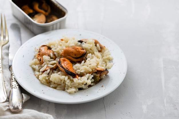 Rice with mussels on small white plate on ceramic background