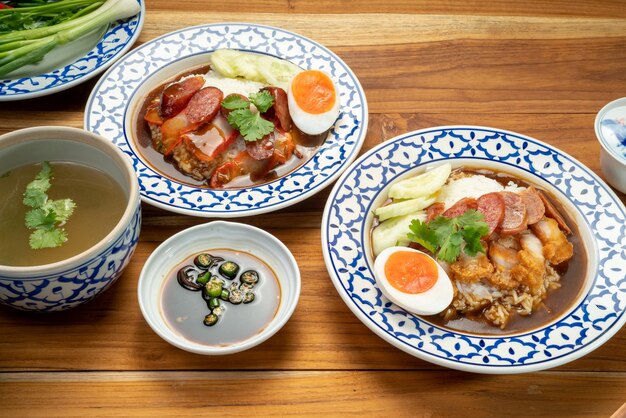 Rice with red roasted pork with sauce and Egg topped in a white dish on wooden table