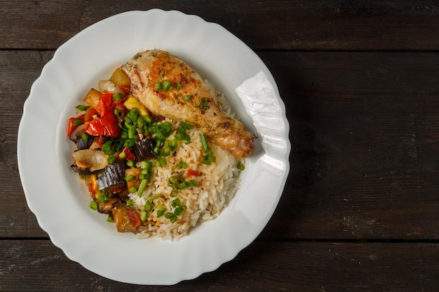 Rice with vegetables in sauce and chicken leg in a white plate on a wooden tablecopy space