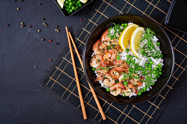 Rice with young green peas, shrimps and arugula in black bowl. Healthy food. Buddha bowl. Top view. Flat lay