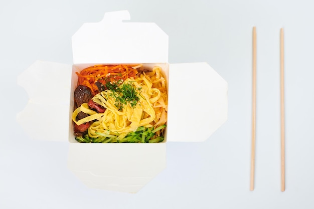 Rice wok with seafood cocktail and vegetables in box and wooden chopsticks isolated on white background, studio. Open takeout box with wok and bamboo sticks. Takeout and takeaway fast food concept