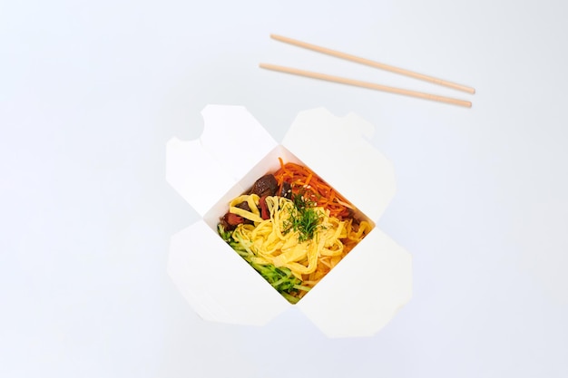 Rice wok with seafood cocktail and vegetables in box and wooden\
chopsticks isolated on white background, studio. open takeout box\
with wok and bamboo sticks. takeout and takeaway fast food\
concept