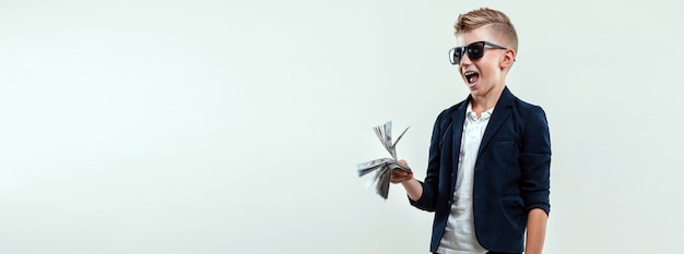 A rich boy on a light background holds a bundle of dollars in his hands. Financial education