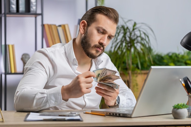 Rich businessman in shirt working on laptop pc counting money cash calculate earnings income profit