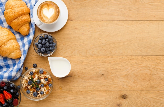 Foto ricca colazione continentale. cornetti francesi croccanti, muesli, tanti frutti di bosco dolci, caffè caldo per i pasti mattutini. delizioso inizio di giornata. vista dall'alto con copia spazio sul tavolo di legno