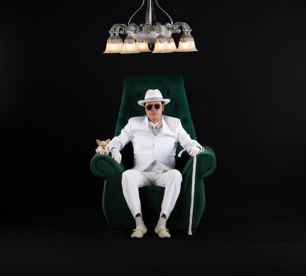 rich gentleman in a white suit sits on a chair black studio background