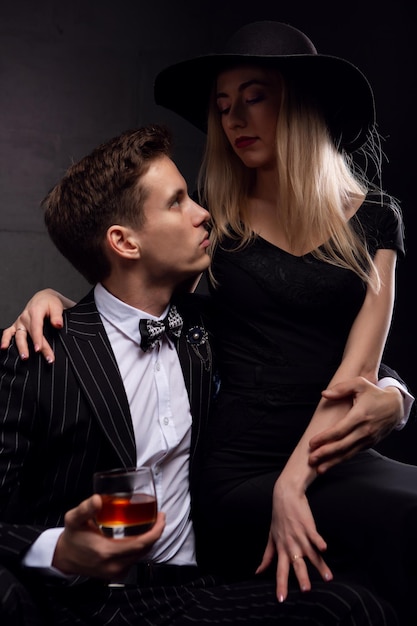 A rich handsome man drinks whiskey with a blonde mistress in the evening