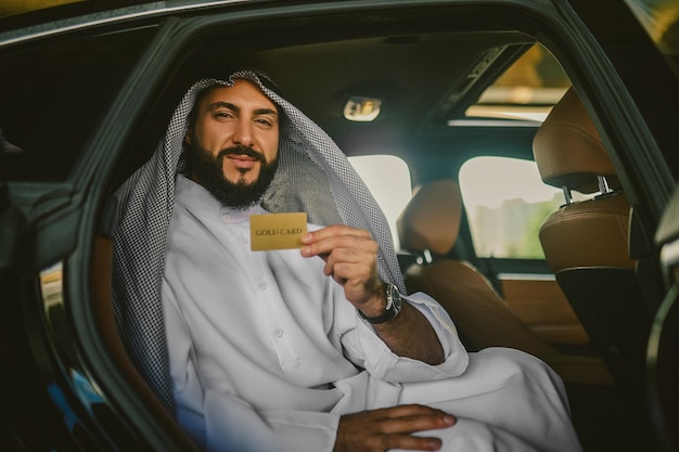 Rich man An arabian man in a traditional clothing in a car holding a credit card