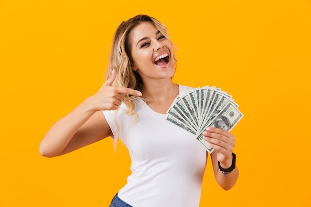 Rich woman in basic clothing holding fan of dollar money, isolated over yellow wall