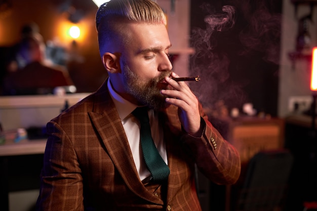 Rich young businessman in suit smokes a cigar