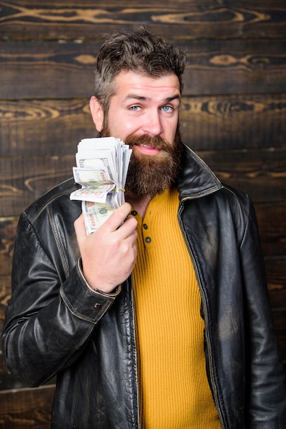 Richness and wellbeing. man brutal bearded hipster wear leather\
jacket and hold cash money. mafia business. illegal profit and\
black cash. guy mafia dealer with cash profit. brutal man has cash\
money.