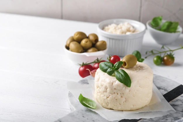 リコッタチーズ自家製リコッタチーズ、バジルガーリックトマトとグリーンオリーブを羊皮紙のペーパーバックに載せ、古いベージュのタイルの上に立つイタリア料理セレクティブフォーカス
