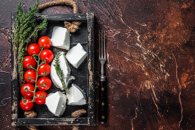 Ricotta cream Cheese in a wooden tray with basil and tomato. Dark background. Top view. Copy space.