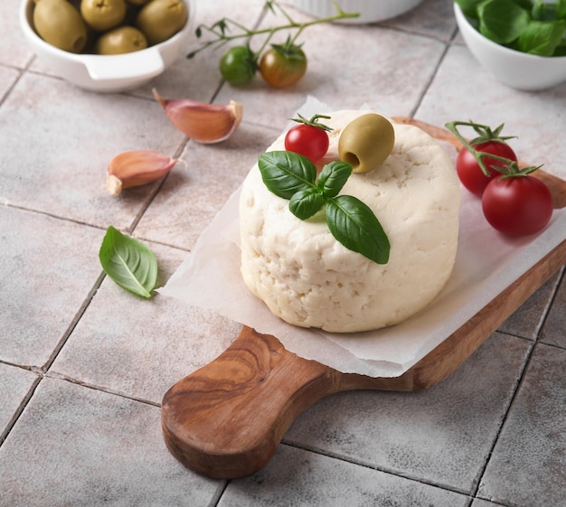 Ricotta kaas zelfgemaakte ricotta kaas met basilicum knoflook tomaten en groene olijven op perkament paperback en staan op oude beige tegels achtergrond italiaans eten selectieve aandacht