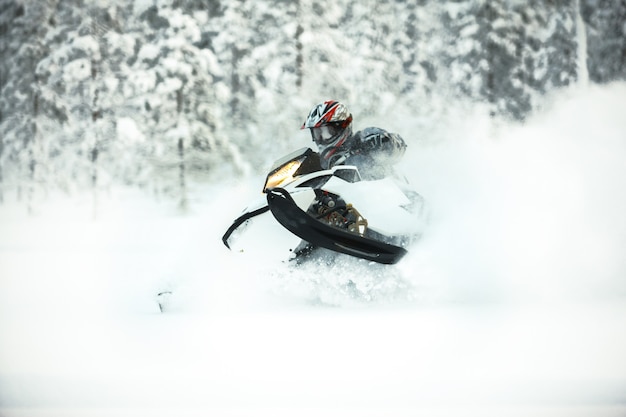 Il pilota in marcia con un casco alla guida di una motoslitta su una neve profonda