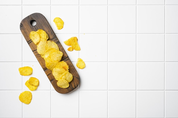 Ridged potato chips on white ceramic squared tile table background top view flat lay with copy space for text