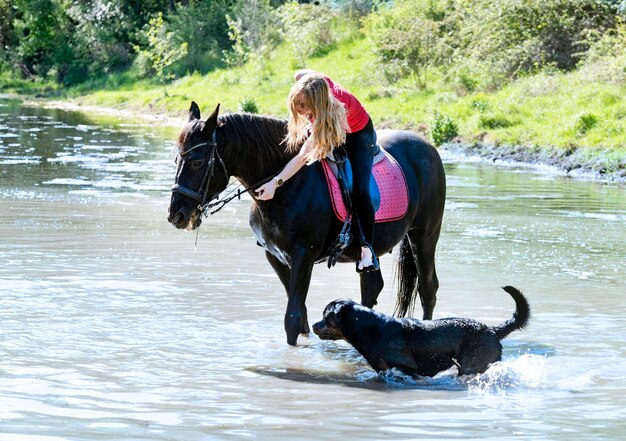 Ragazza di equitazione cane e cavallo nel fiume