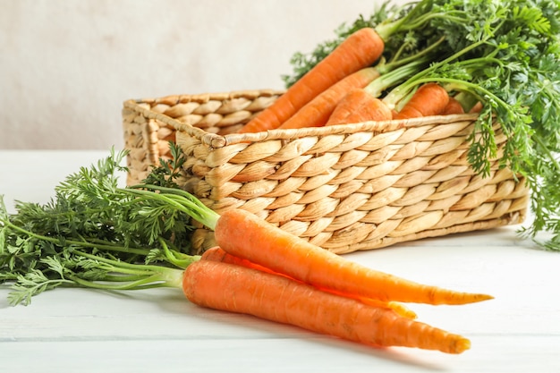 Rieten mand met rijpe wortelen op houten tafel, close-up