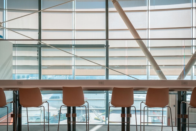 Rij stoelen met houten aanrechttafel op vensterglas met luchthaven in lounge