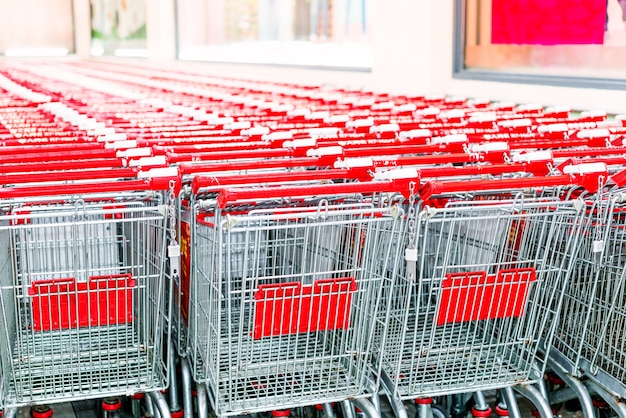 Rij van boodschappenwagentjes met rode handvatten op avond onscherpe achtergrond dichtbij ingang van supermarkt in de winter