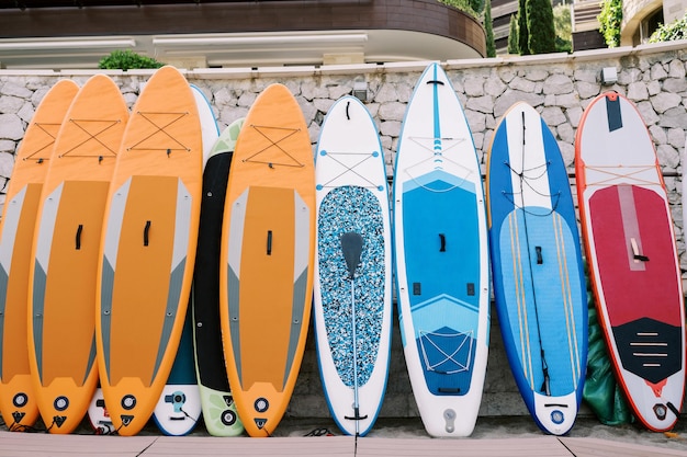 Rij van kleurrijke surfboards staat bij een stenen hek op het strand