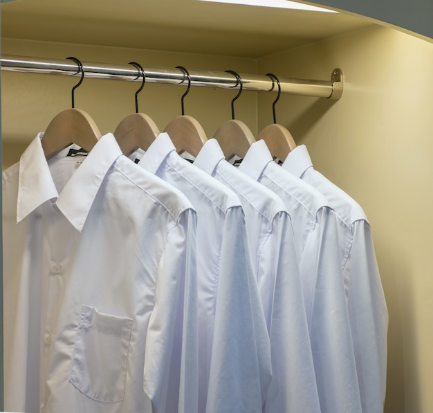Rij van witte overhemden die op kleerhanger in garderobe hangen