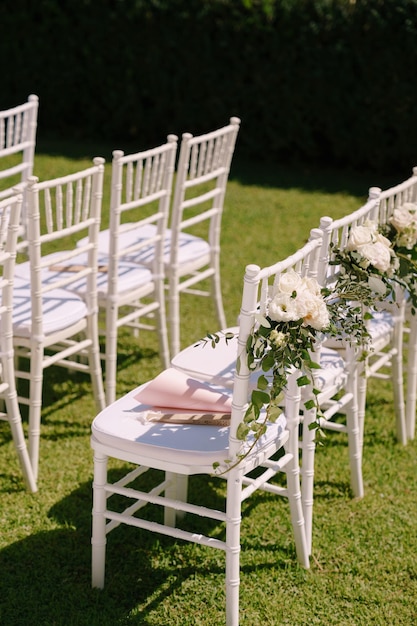 Rij witte stoelen versierd met boeketten bloemen staat op een groen gazon