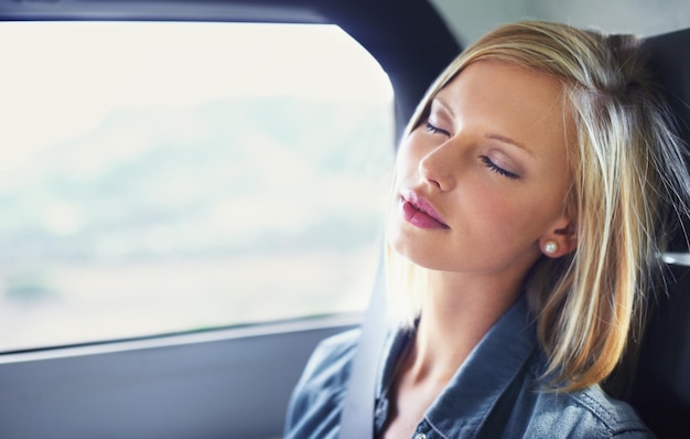 Rijden in luxe. Shot van een aantrekkelijke jonge vrouw in slaap op de achterbank van een auto tijdens een roadtrip.