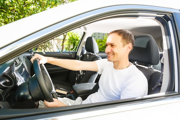 Rijden in zijn nieuwe auto. Zijaanzicht van een knappe jongeman die in zijn auto rijdt en glimlacht