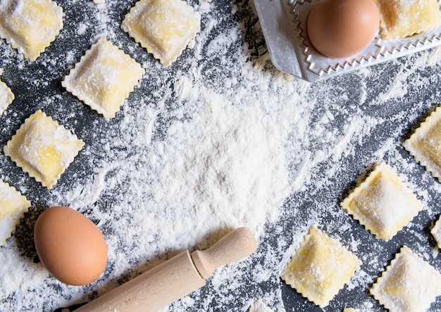 Rijen van rauwe zelfgemaakte ravioli op een donkere achtergrond met ingrediënten, close-up en bovenaanzicht