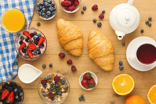 Rijk continentaal ontbijt. Franse knapperige croissants, muesli, yoghurt, melkkan, theepot, kop warme zwarte koffie en veel zoete bessen voor een smakelijke ochtendmaaltijd. Heerlijk begin van de dag, bovenaanzicht