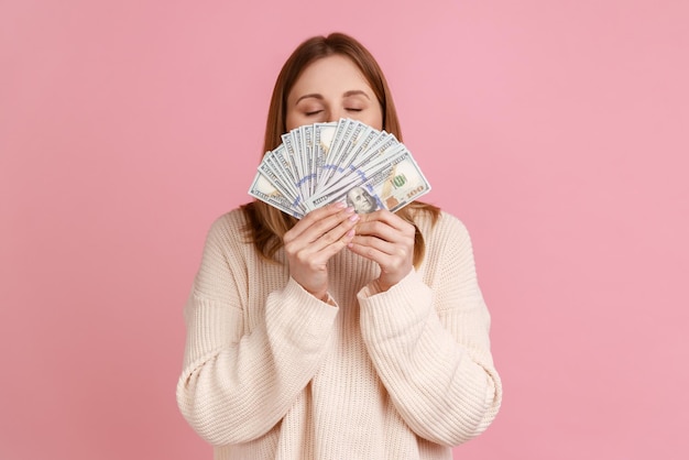 Rijke hebzuchtige vrouw die een grote fan van dollarbiljetten vasthoudt en geld ruikt met een tevreden uitdrukking