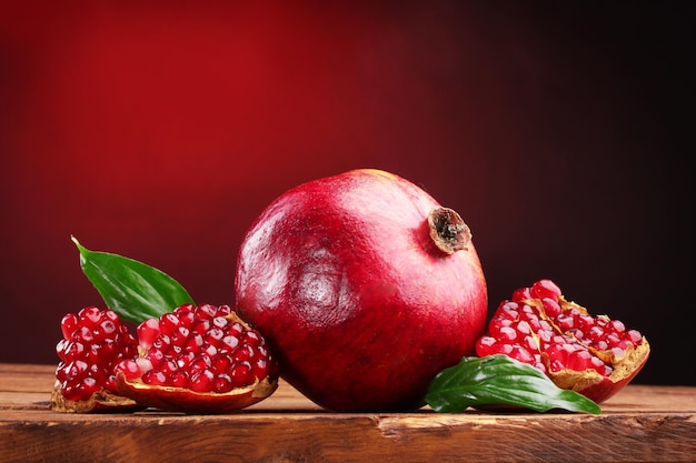 Rijp granaatappelfruit met bladeren op houten tafel op rode achtergrond