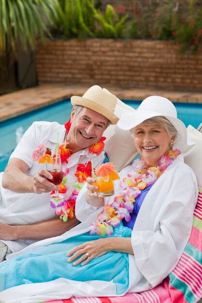 Rijp paar dat een cocktail drinkt naast het zwembad