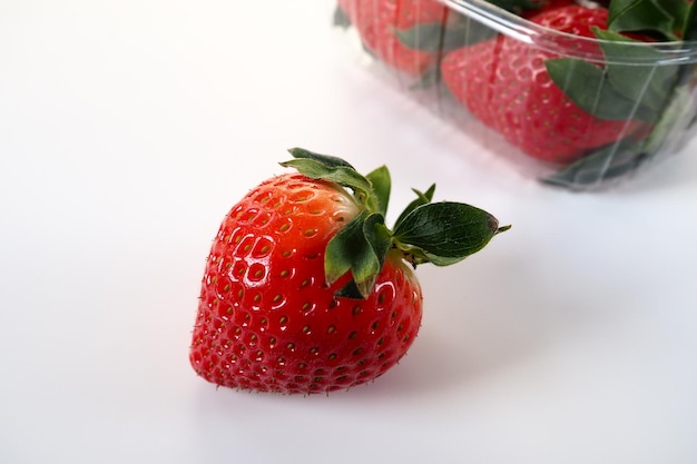 Rijpe aardbeien in een plastic verpakking op een witte achtergrond Heerlijke verse bessen in een container te koop aan klanten Voedsel vers houden Gezonde voeding Een aardbei uit de container getrokken